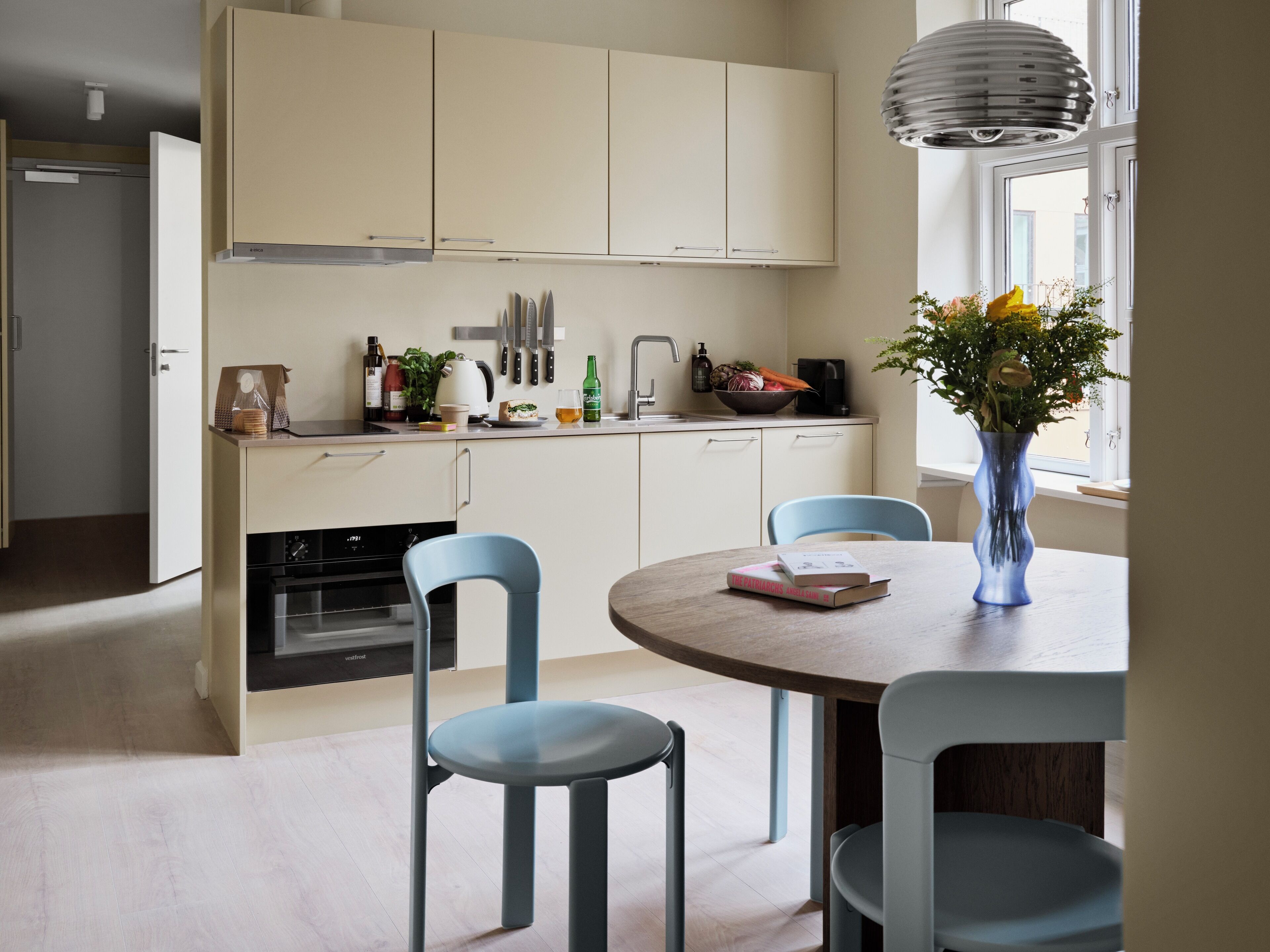 A modern kitchen with white cabinets, a dining table with blue chairs, and a vase with flowers on the table.