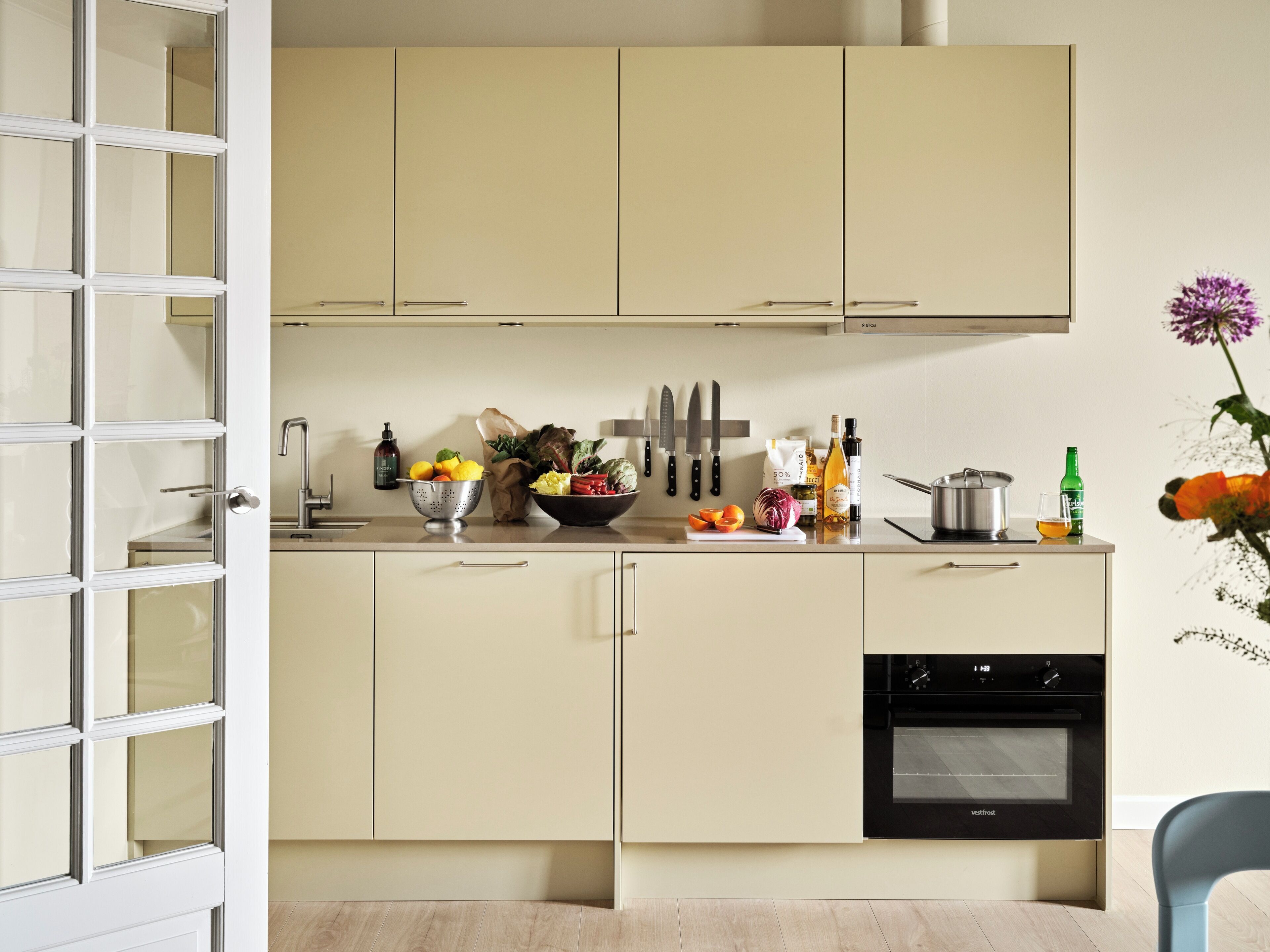 Una cocina moderna con armarios de tonos claros, un lavamanos de acero inoxidable y un horno negro.
