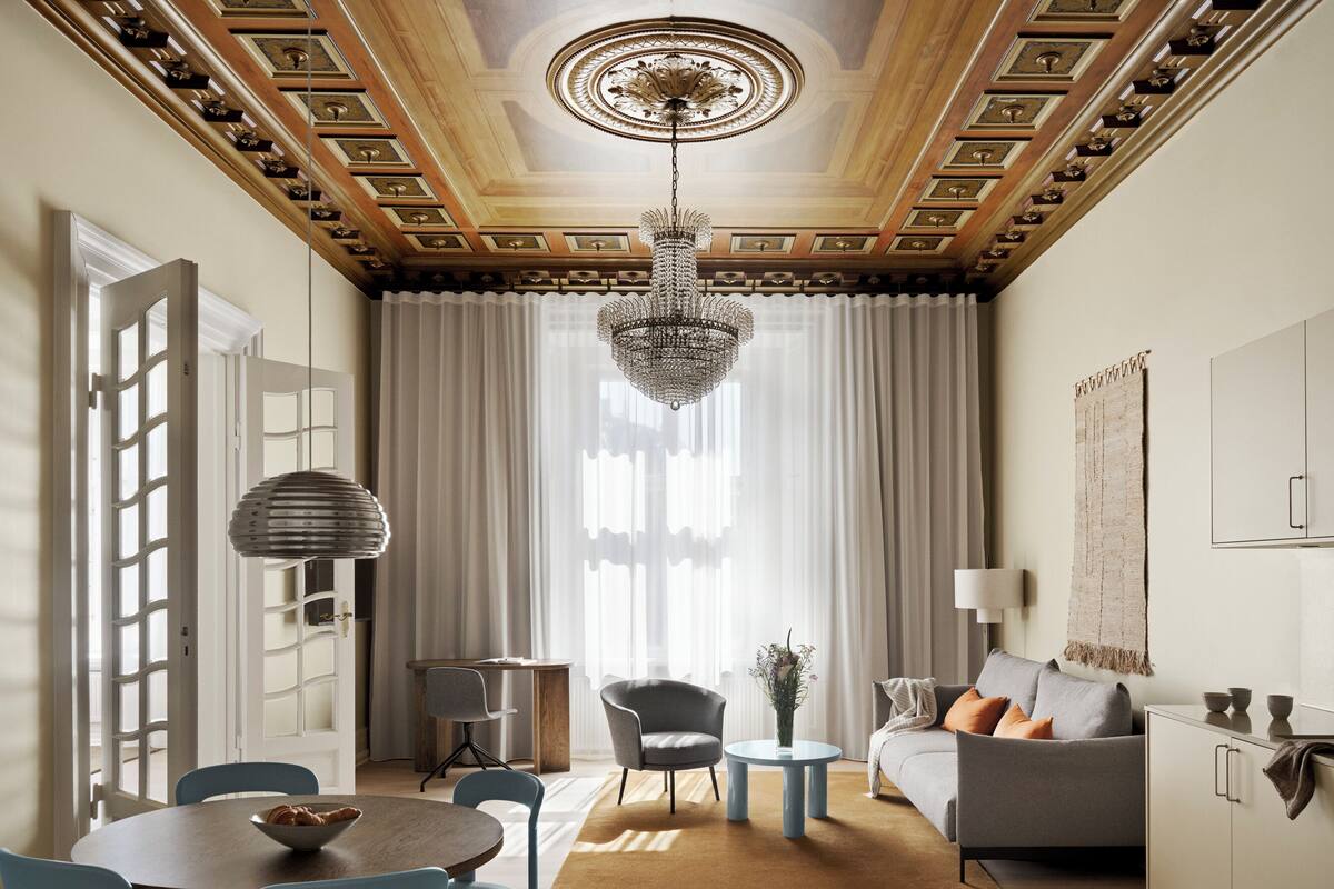 Een moderne woonkamer met een eethoek, een kroonluchter en uitzicht op de omgeving door grote ramen.