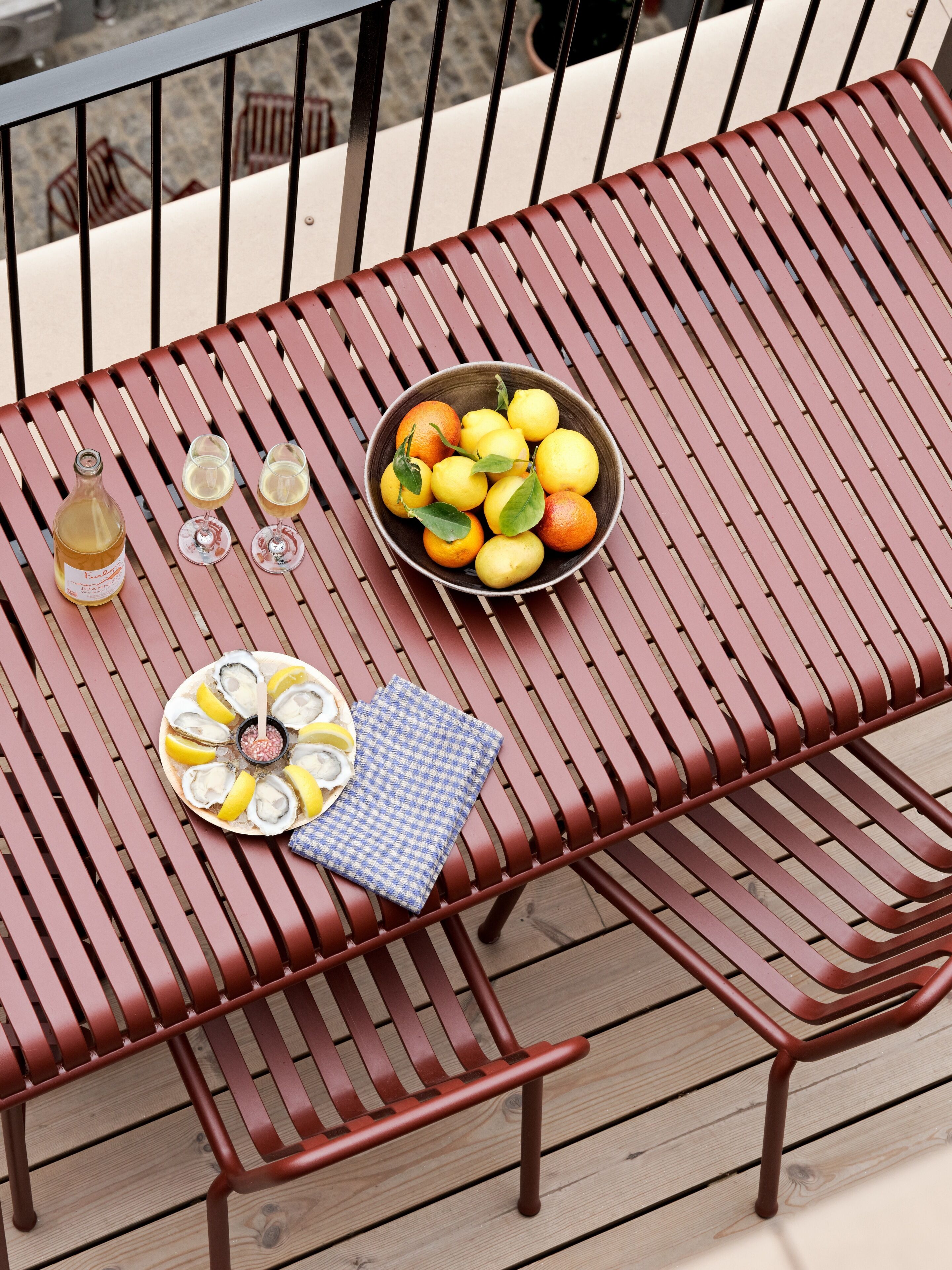 A metal table with a bowl of lemons and oranges, a bottle of wine, and two glasses on it.