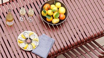 A metal table with a bowl of lemons and oranges, a bottle of wine, and two glasses on it.