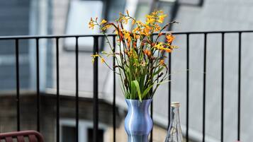 A round table with a dessert, a bottle of red wine, and a vase with flowers on a balcony.