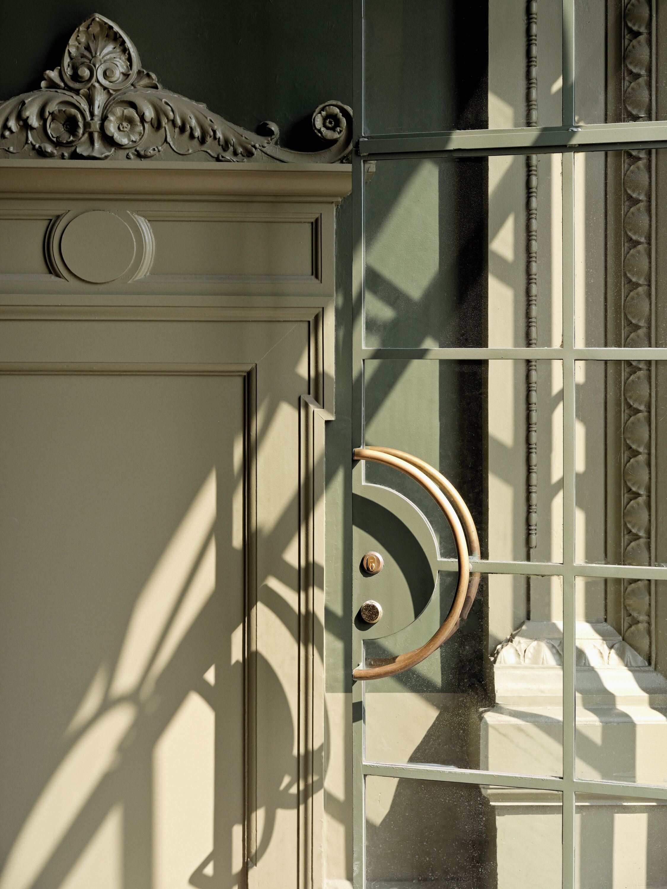 A door with a decorative metal handle and a circular design, set in a building with a textured wall.