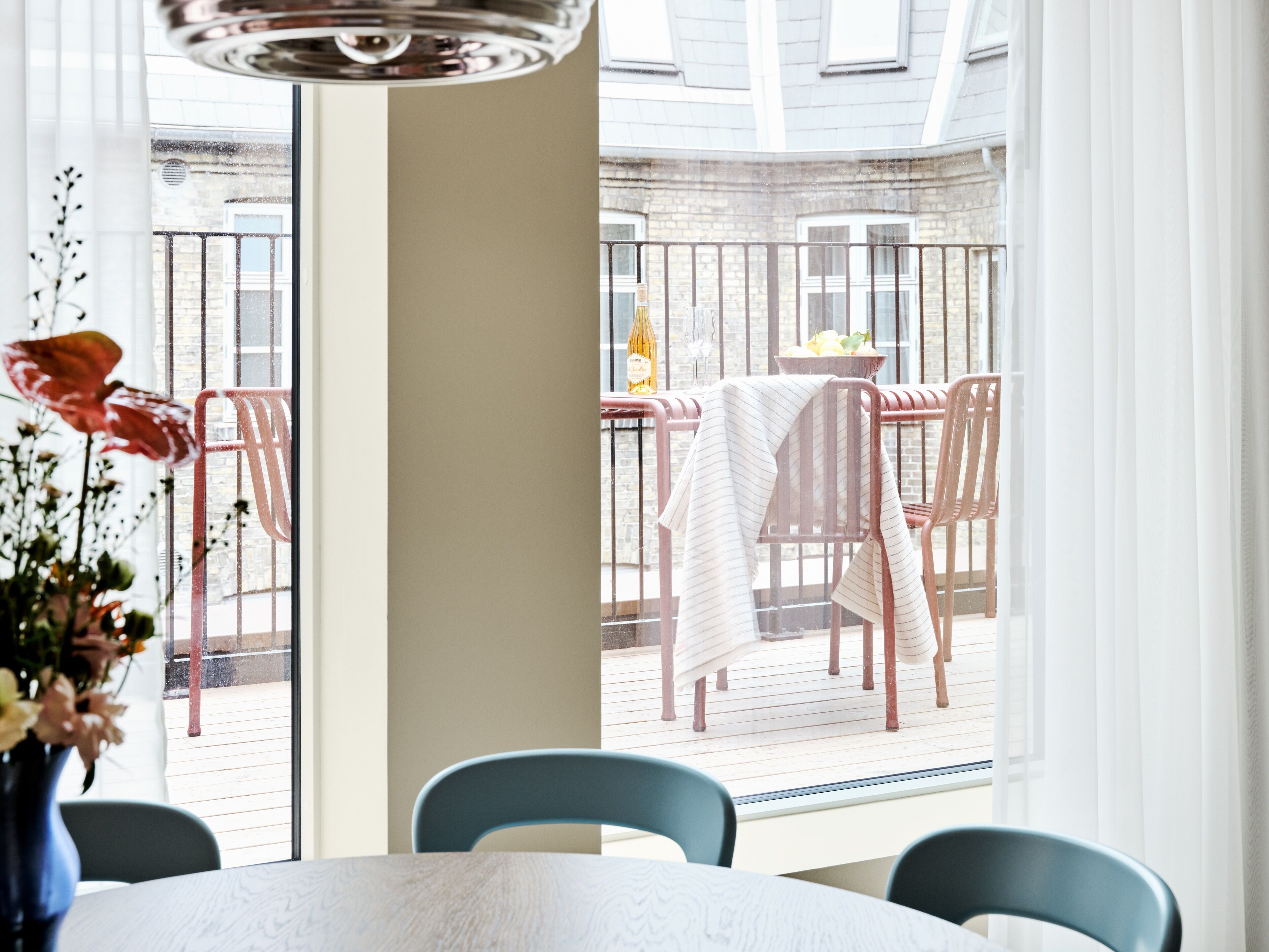 A dining area with a table and chairs, a view of the outside balcony, and a window with a view of the building.