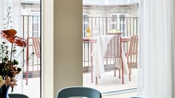 A dining area with a table and chairs, a view of the outside balcony, and a window with a view of the building.
