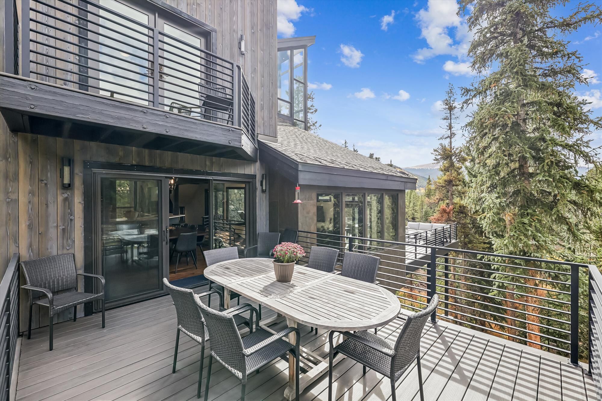 A modern outdoor patio with a round table and chairs, a stone wall, and a view of trees and mountains.