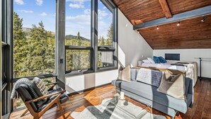 Un dormitorio moderno con un ventanal grande, techo de madera y una cama con muchas almohadas.
