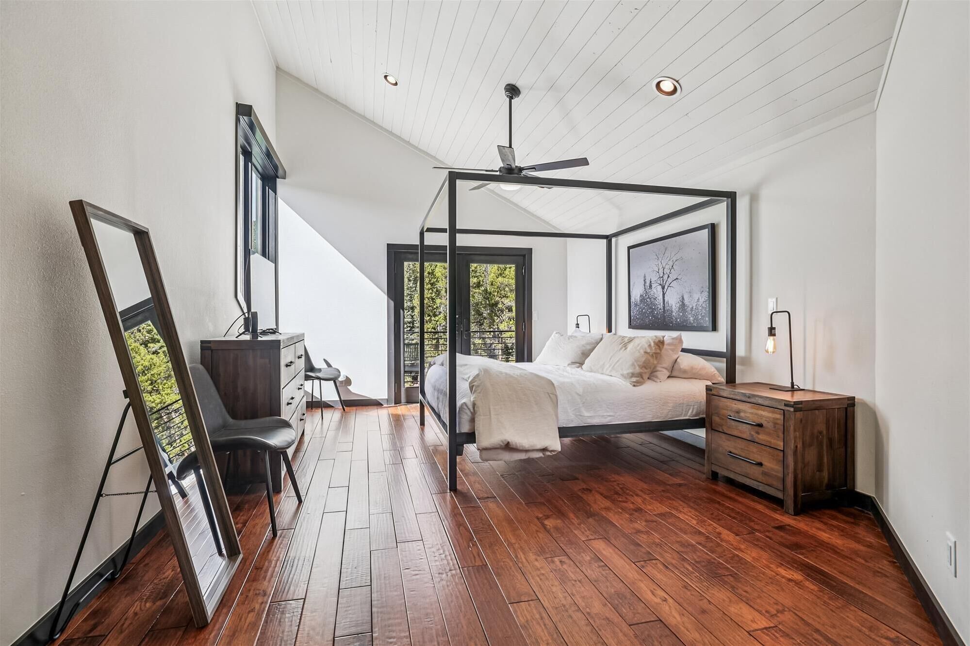 Une chambre à coucher avec un lit à baldaquin, un plancher en bois, un ventilateur de plafond et une table de chevet avec une lampe.