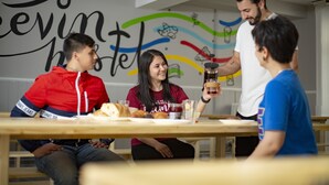 A group of people sitting at a wooden table with food and drinks, in a room with a colorful wall mural. - Leevin Hostel Mountjoy (Dublin)