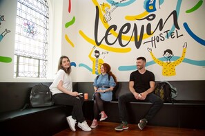 Three people sitting on a bench in a hostel with a colorful wall mural and a window with bars.