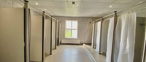 A corridor with a row of individual shower stalls, a window providing natural light, and a tiled floor.
