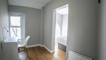 A modern room with a desk, chair, and a view of a bedroom through an open doorway.