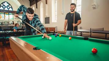 A pool table in a room with wooden flooring and arched windows.