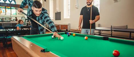 A pool table in a room with wooden flooring and arched windows.