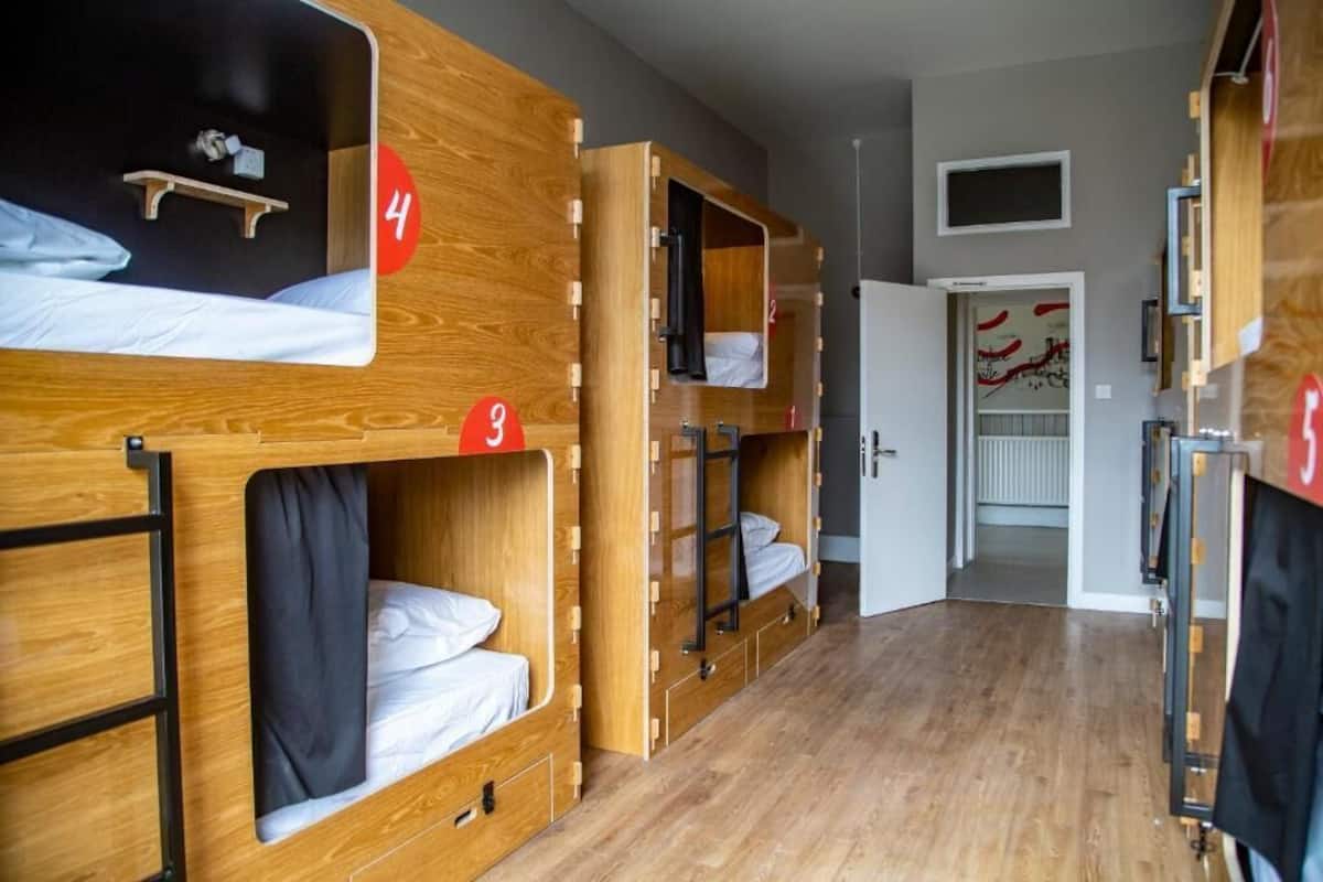 Une chambre de type dortoir, avec des lits superposés, des portes numérotées et un couloir menant à une porte aux motifs rouges et blancs.