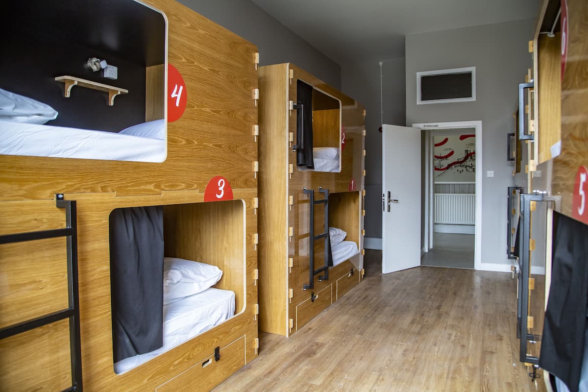 Une chambre de type dortoir, avec des lits superposés, des panneaux numérotés indiquant le numéro de la chambre et une porte donnant accès à une salle de bain.