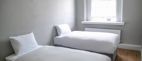 A room with two beds, a window, and a radiator.