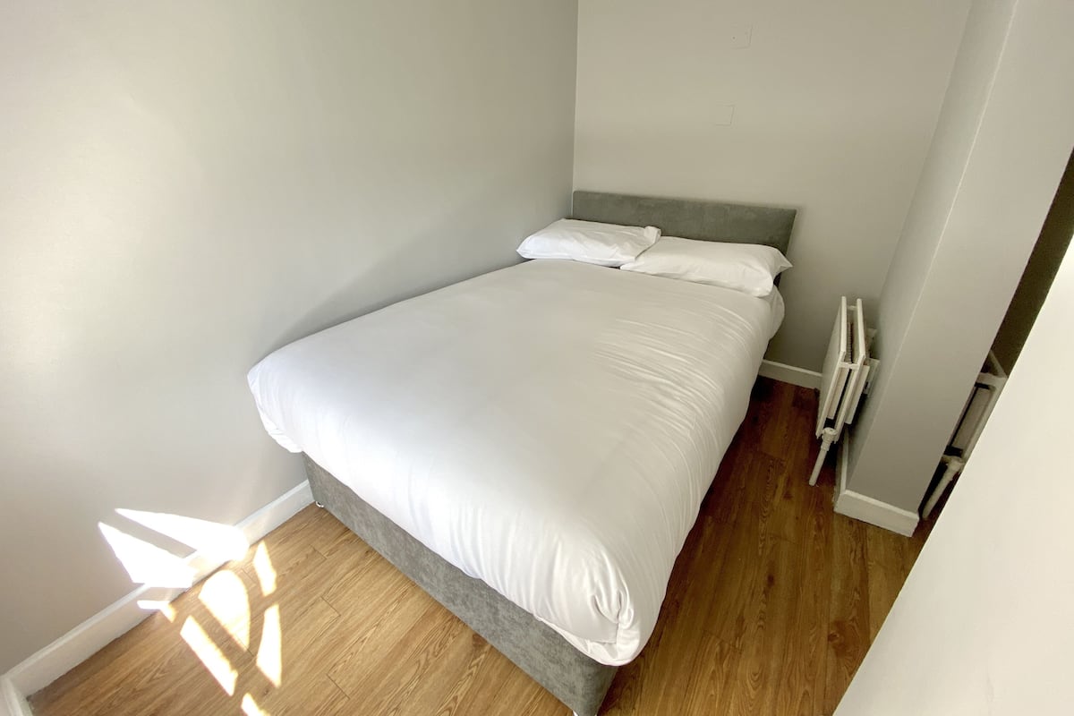 Un petit lit bien fait, dans une pièce au plancher en bois et aux murs blancs.