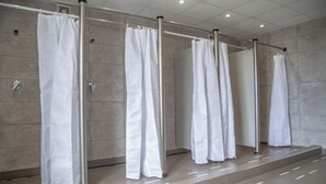 A row of white shower curtains in a modern bathroom with tiled walls and floors. - Leevin Hostel Mountjoy (Dublin)