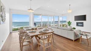 Un vaste espace dédié à la salle à manger, offrant une vue sur l’océan, avec des chaises en bois, une grande table et un luminaire moderne.