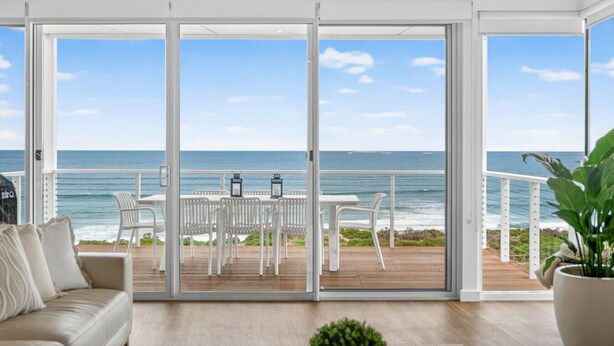 Un salon moderne doté d’une grande porte-fenêtre coulissante donnant sur un balcon avec vue sur l’océan.