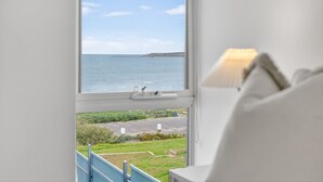 Une chambre dotée d’une grande fenêtre donnant sur la côte, d’un lit et d’une table de chevet avec une lampe.