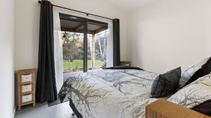 Un dormitorio con una cama grande, una mesita de noche de madera, un armario pequeño y una ventana con cortinas.
