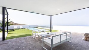 A modern outdoor patio with a pool, seating, and a view of the ocean.
