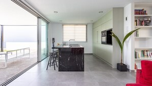 A modern kitchen with a central island, a dining area, and a large window overlooking a balcony.
