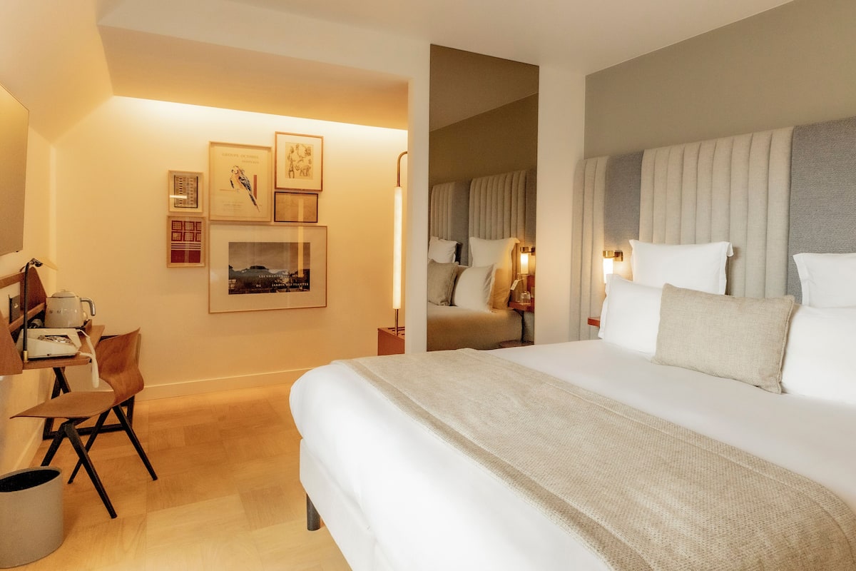 Une chambre d’hôtel avec un grand lit, un bureau avec une chaise et des tableaux encadrés au mur.