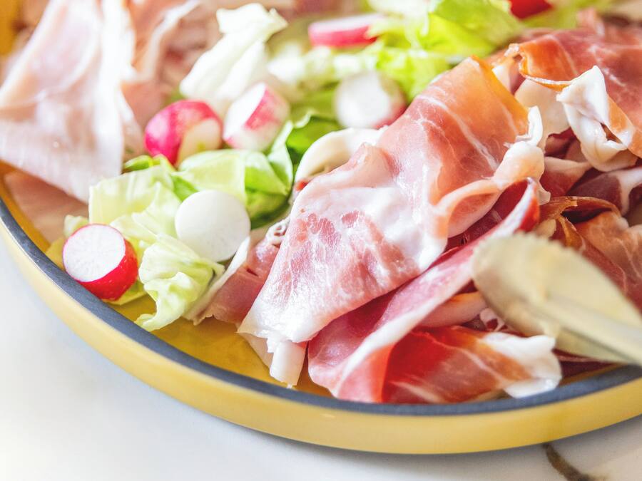 Un plato con varios alimentos, entre ellos lechuga, rábanos y láminas de carne.