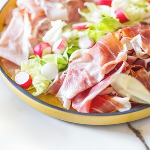 A plate with various food items including lettuce, radishes, and slices of meat. - Hôtel Pilgrim (Paris)