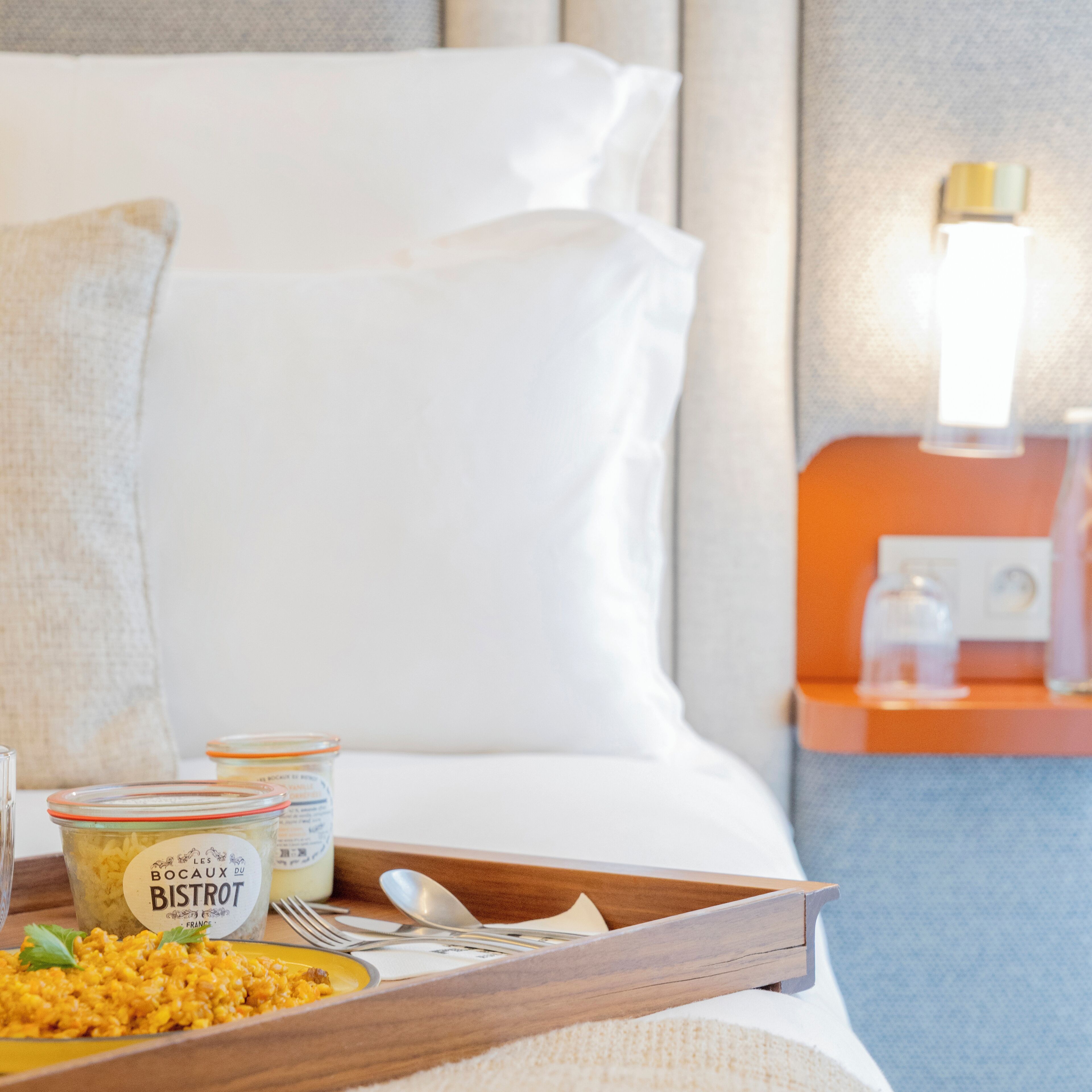 Una habitación de hotel con una cama bien hecha, una bandeja con provisiones para el desayuno y una mesita de noche con una lámpara.