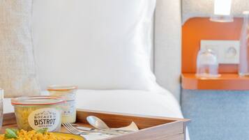 Una habitación de hotel con una cama bien hecha, una bandeja con provisiones para el desayuno y una mesita de noche con una lámpara.