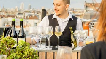 Una persona sentada a una mesa con botellas y copas de vino, con vistas a un paisaje urbano.