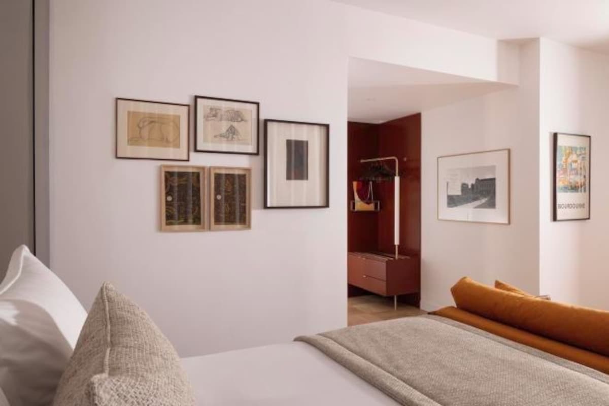 A modern bedroom with a bed, a sofa, and a wardrobe. There are framed pictures on the wall.