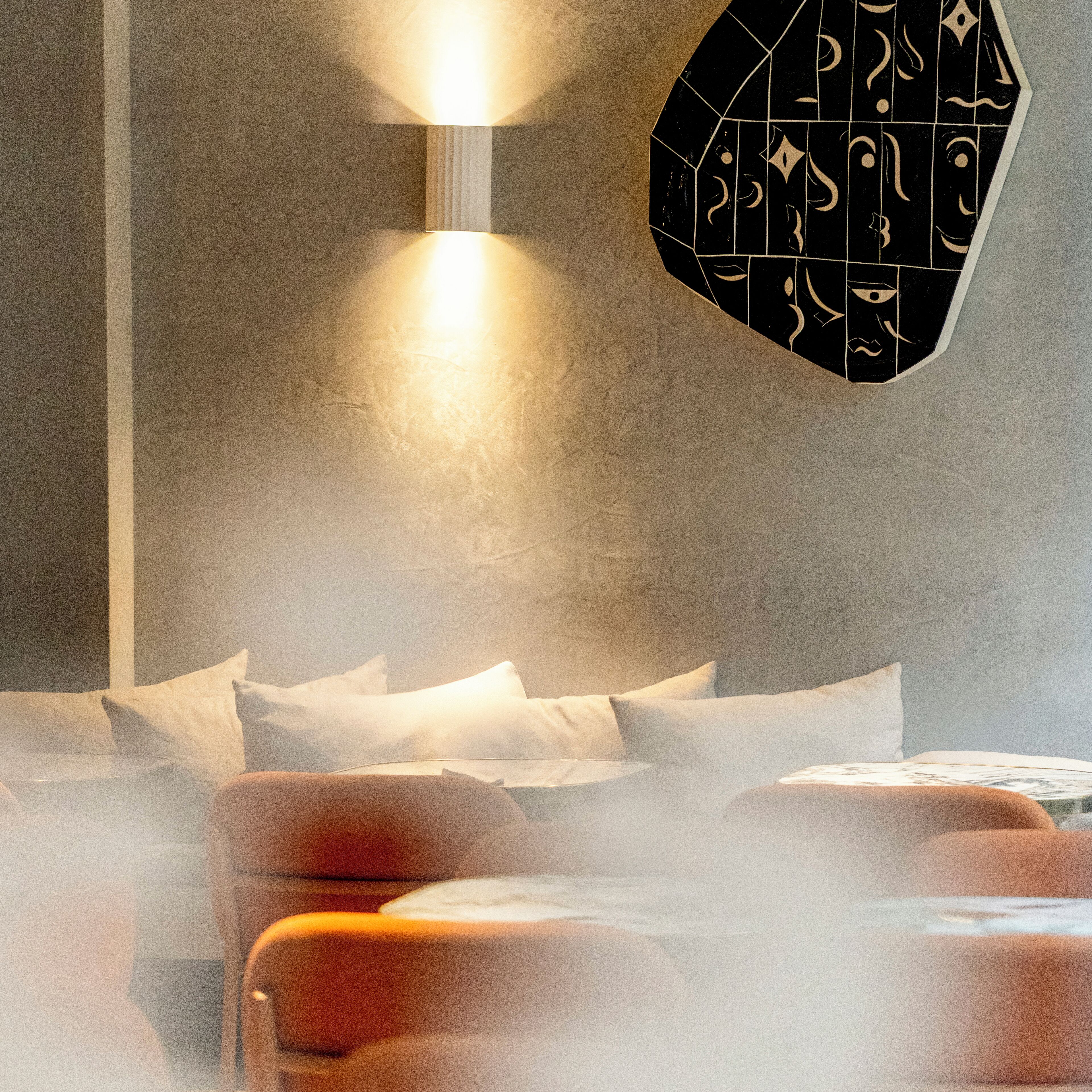 Een kamer met een bed, kussens en een wandlamp.