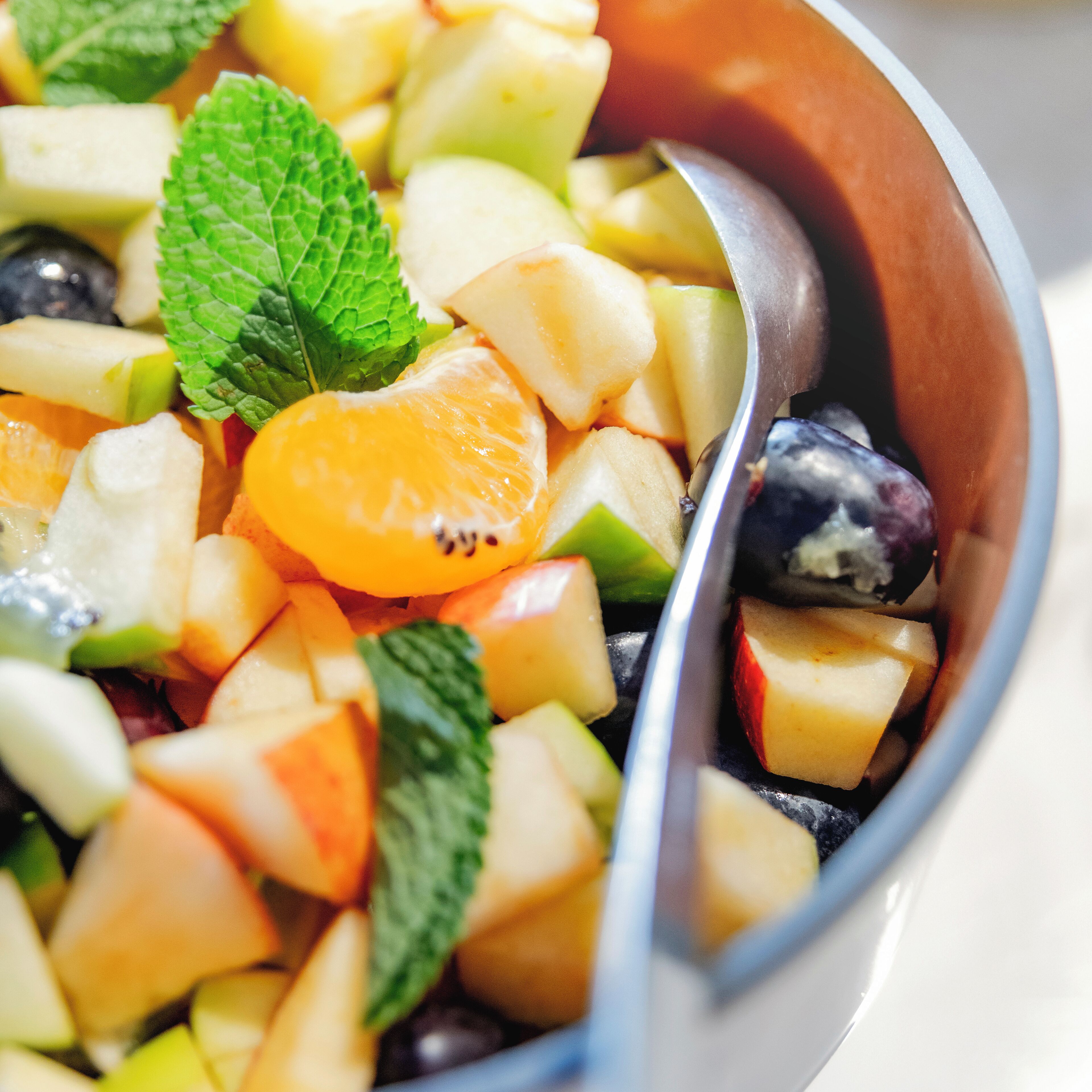 A bowl of fruit salad with various fruits and mint leaves.