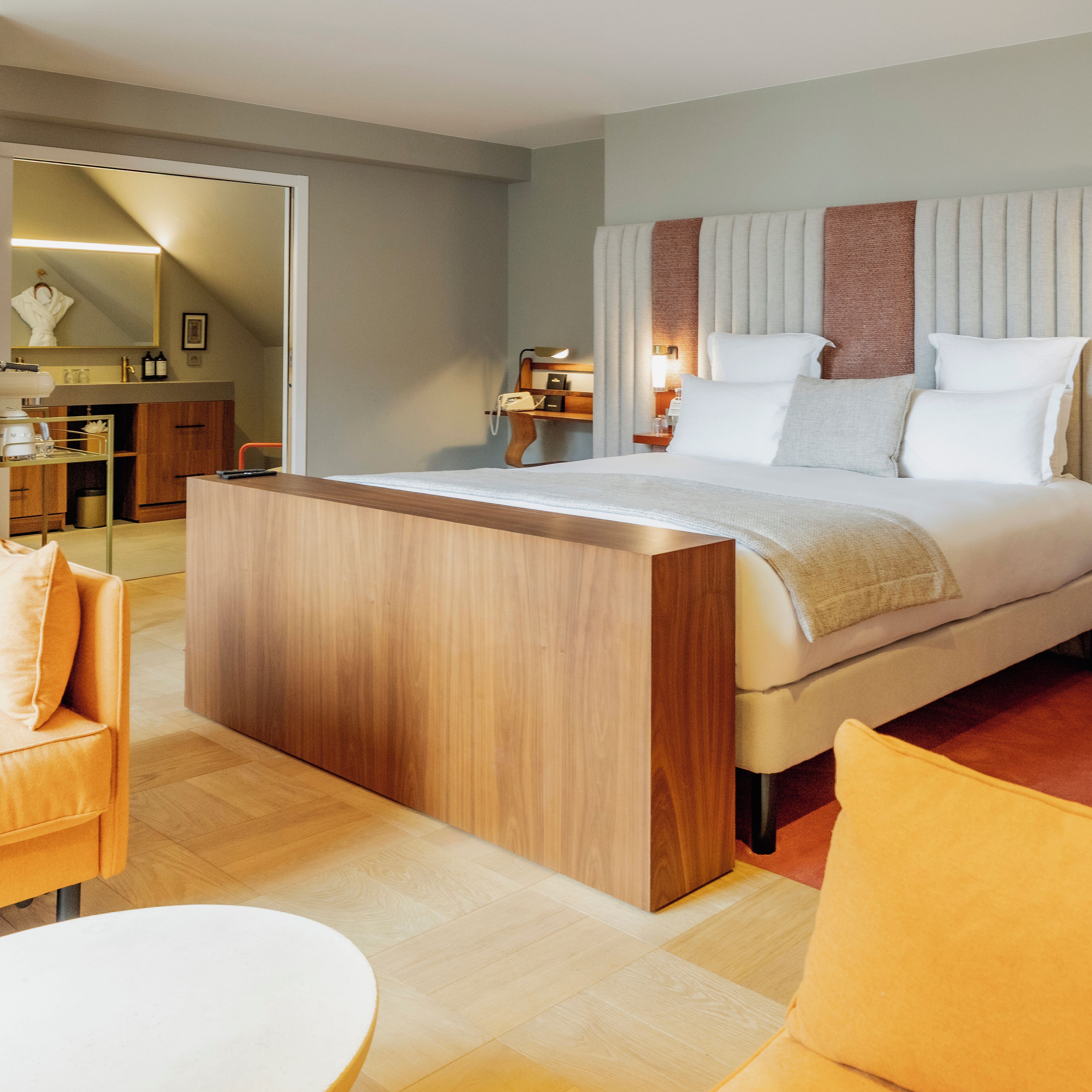 Una habitación de hotel moderna con una cama grande, una mesita de noche de madera, un escritorio pequeño y una silla.
