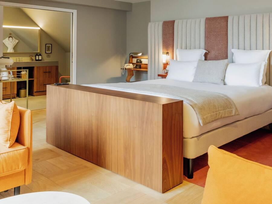 Una habitación de hotel moderna con una cama grande, una mesita de noche de madera, un escritorio pequeño y una silla.