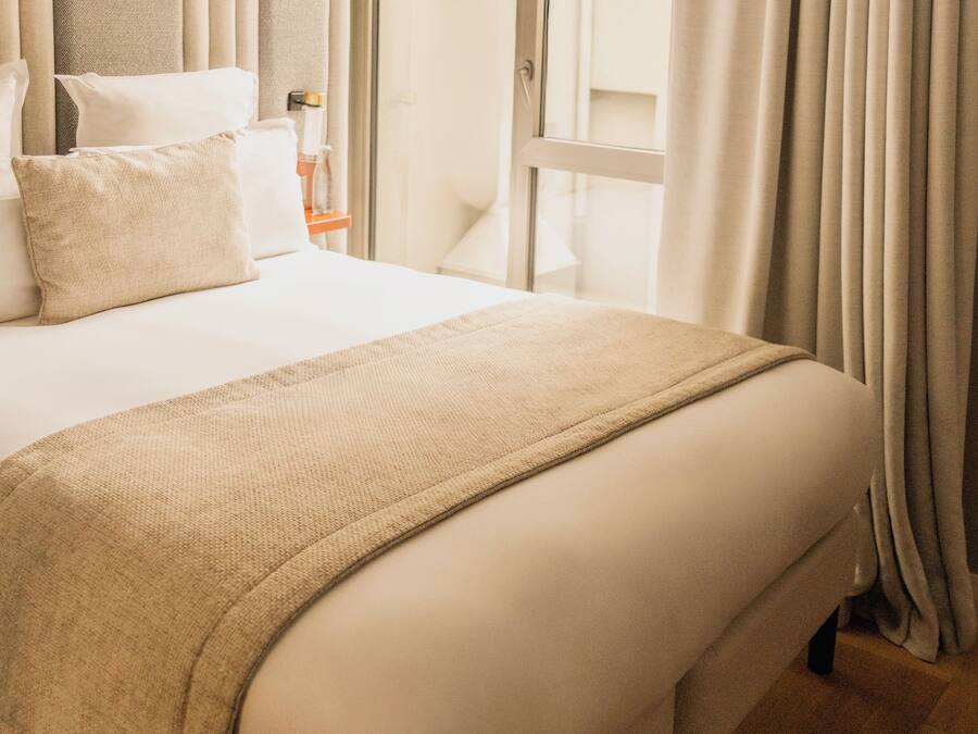 Habitación de hotel con una cama grande, una mesita de noche, una ventana con cortinas y vistas al exterior.