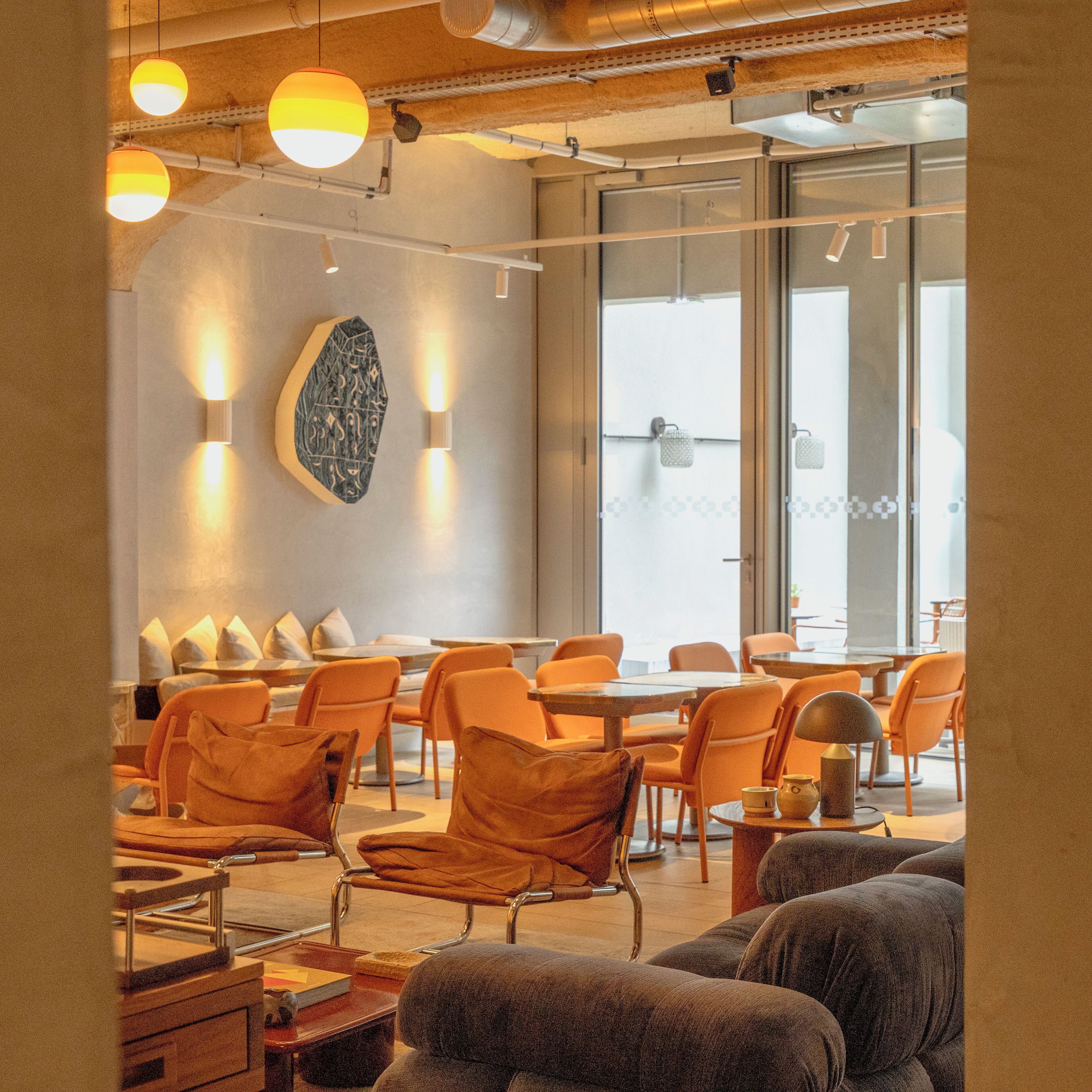 A modern interior with orange chairs, tables, and pendant lighting.