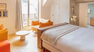 A hotel room with a large bed, a small table, a sofa, and a balcony with a view.