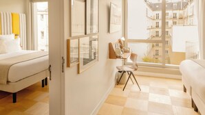 A hotel room with a bed, a desk, a chair, and a large window with a view of buildings. - Hôtel Pilgrim (Paris)