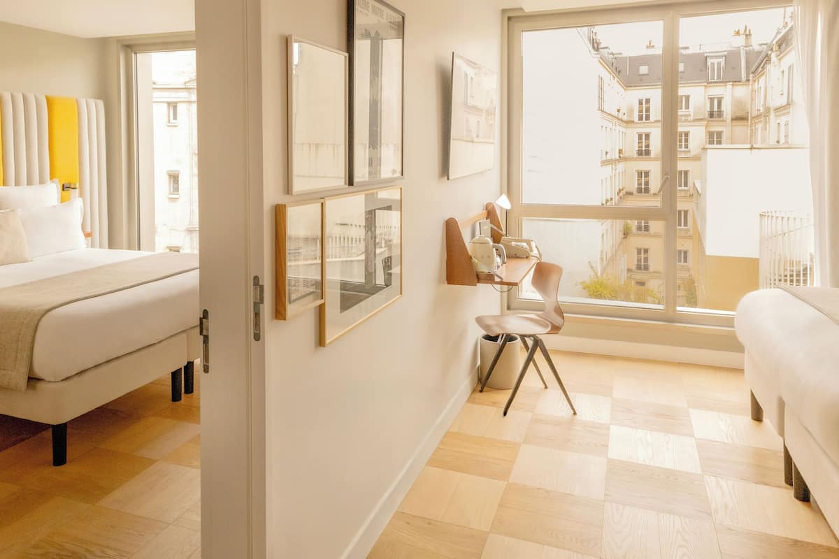 Une chambre d’hôtel avec un lit, un bureau, une chaise et une grande fenêtre donnant sur des immeubles.