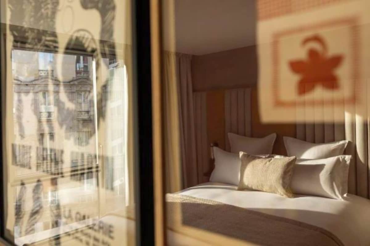 A hotel room with a bed, pillows, and a window with a view of a building.