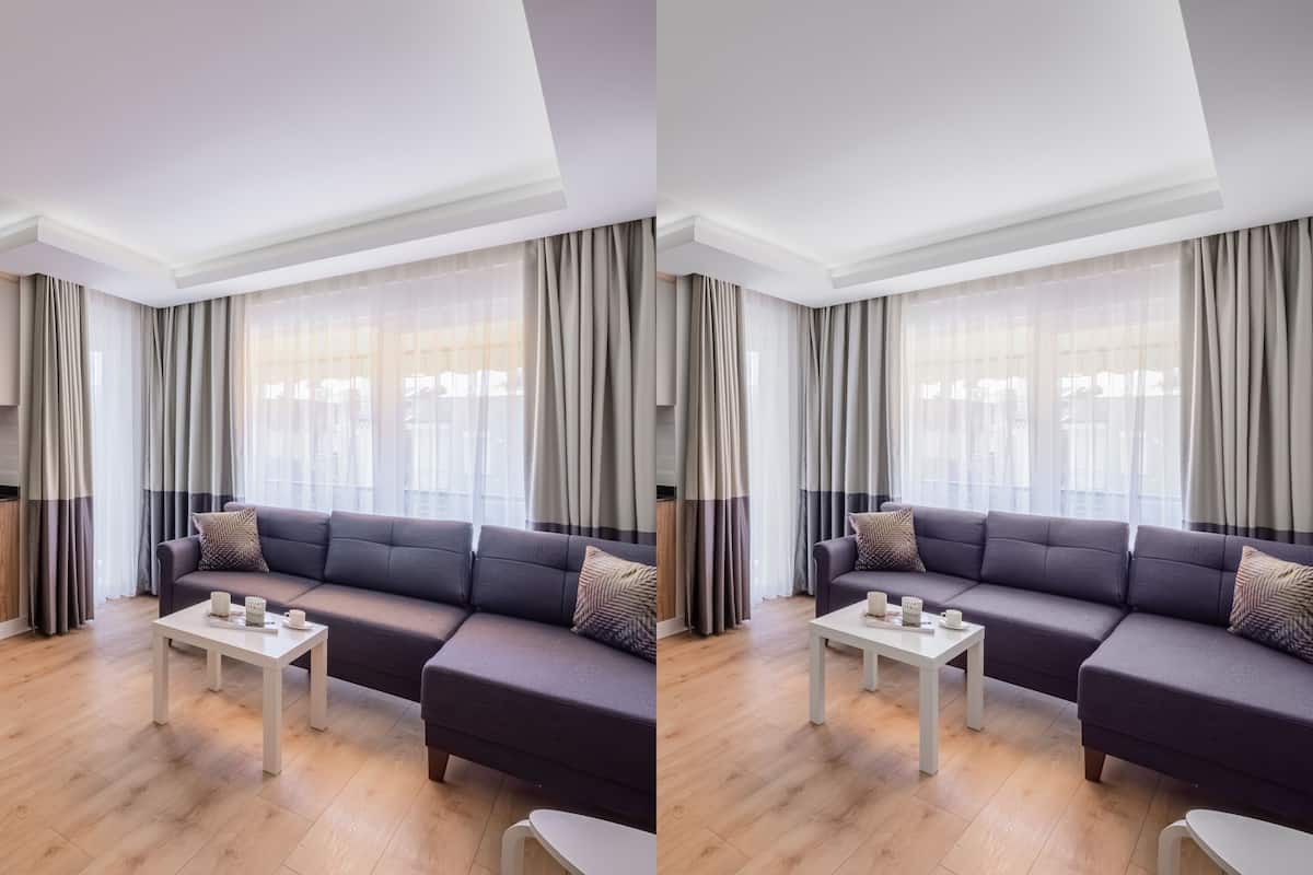 A modern living room with a dark sofa, a white coffee table, and sheer curtains.