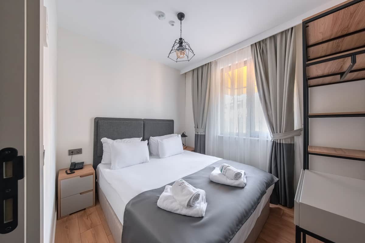 A modern hotel room with a large bed, a bedside table with a phone, and a wardrobe with a wooden finish.