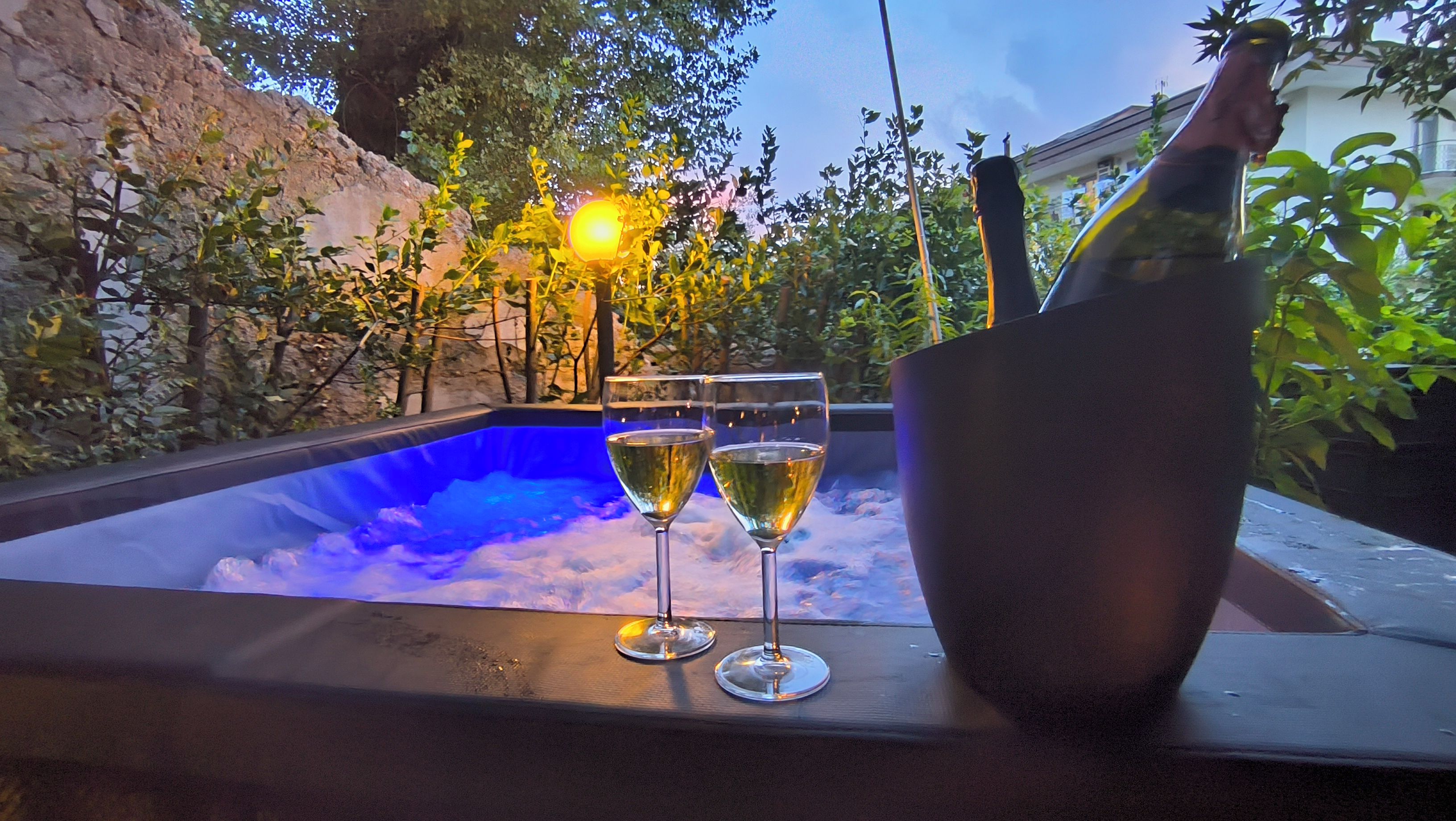 A hot tub with two glasses of white wine and a bottle of champagne.