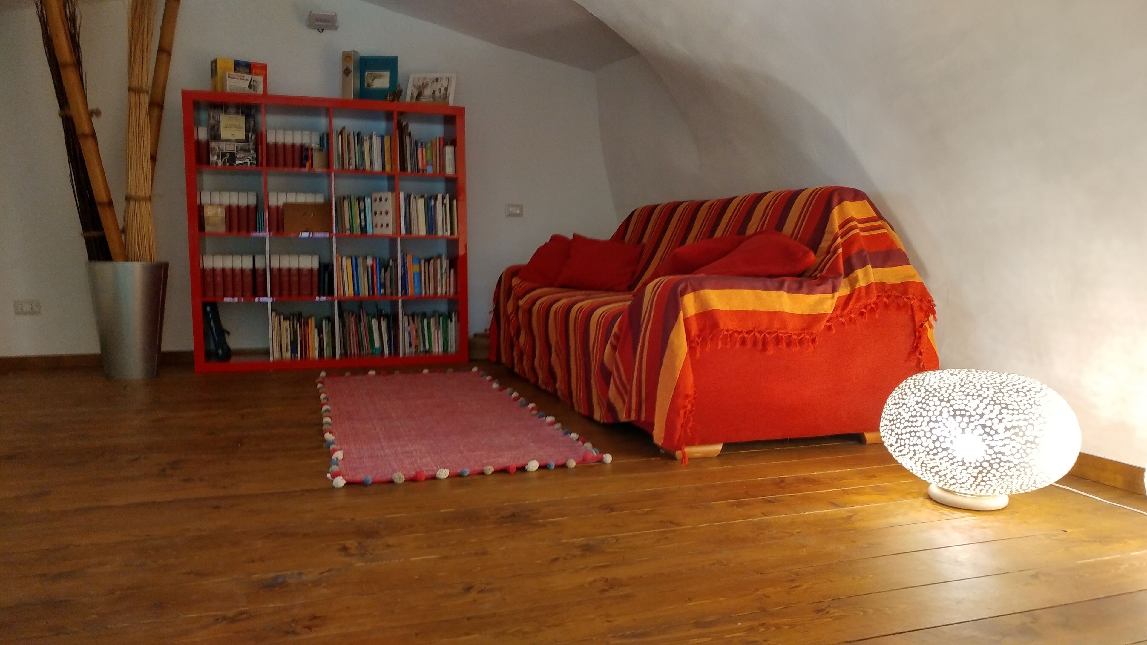 Une pièce chaleureuse avec un plancher en bois, un canapé rouge, une bibliothèque et une lampe décorative.